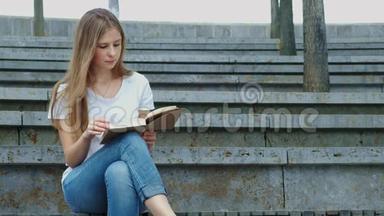 公园里年轻漂亮的女孩<strong>正在看书</strong>。 一个学生<strong>正在</strong>学习一本书，翻页。 混凝土上的裂缝